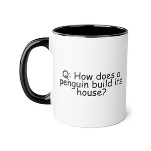 May include: White coffee mug with a black rim and handle. The mug has black text that reads "Q: How does a penguin build its house?"