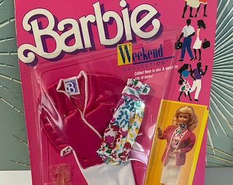 Op de afbeelding: Barbie Weekend Collection kledingset met een roze jasje, een witte rok, een bloemetjesprint top en witte hakken. De verpakking bevat een pop die de outfit draagt.