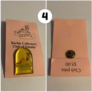Op de afbeelding: Een gouden pin met een rood-witte afbeelding van een vrouw in een jurk. De pin is op een roze kaart met de tekst "Barbie Collectors Club of Omaha" en "Club pins &euro; 0,00".