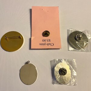 Op de afbeelding: Vier verschillende pins, twee gouden en twee zilveren, met een prijskaartje met de tekst "Club Pins &euro; 5,00".