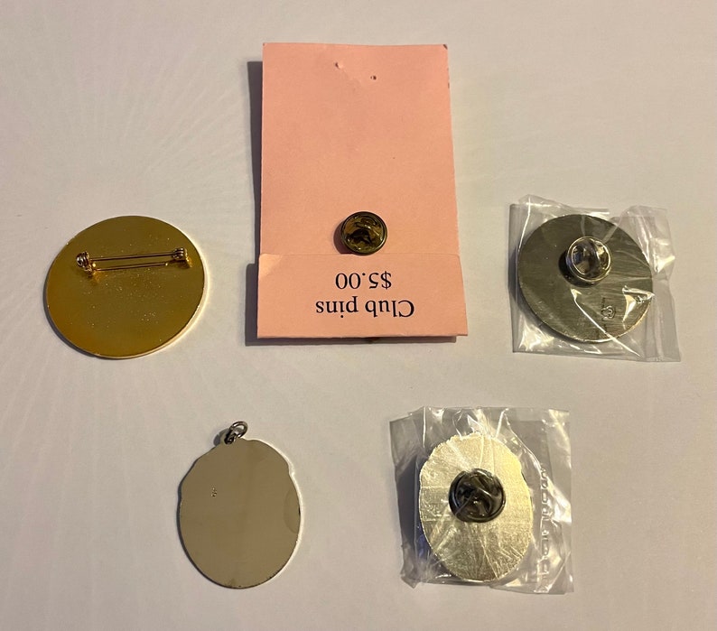 Op de afbeelding: Vier verschillende pins, twee gouden en twee zilveren, met een prijskaartje met de tekst "Club Pins &euro; 5,00".