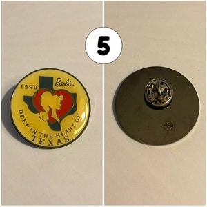 Op de afbeelding: Een gele en rode emaille-pin met een gestileerde omtrek van de staat Texas met de tekst "Deep in the Heart of Texas" en "Barbie" boven de staat. De pin bevat ook het jaar "1990". De achterkant van de pin is zilverkleurig met een pin.
