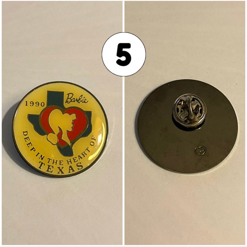 Op de afbeelding: Een gele en rode emaille-pin met een gestileerde omtrek van de staat Texas met de tekst "Deep in the Heart of Texas" en "Barbie" boven de staat. De pin bevat ook het jaar "1990". De achterkant van de pin is zilverkleurig met een pin.