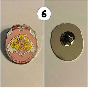 Op de afbeelding: Een roze en witte emaille pin met een cartoonbruid met blond haar en een witte sluier. De pin heeft de tekst "Barbie Wedding Dreams" en "1992" aan de voorkant. De achterkant van de pin is zilver met een pin achterkant.