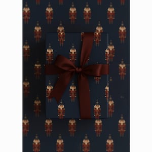 May include: A wrapped gift box with a dark blue background and a repeating pattern of toy soldiers in red and gold. The box is tied with a dark red satin ribbon and bow, creating a festive and elegant presentation.
