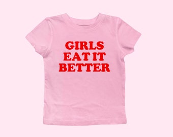 May include: Pink t-shirt with the text "GIRLS EAT IT BETTER" in red.