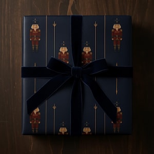 May include: Dark blue gift wrap featuring a repeating pattern of toy soldiers in red and gold. The gift is tied with a dark blue velvet ribbon and bow. The wrapping paper is on a dark wood surface.