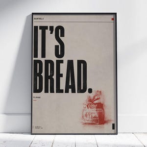 Könnte beinhalten: Ein rechteckiges gerahmtes Poster mit hellbeigem Hintergrund und einem dünnen schwarzen Rahmen. Der Text IT'S BREAD. erscheint in einer großen, fetten, schwarzen serifenlosen Schrift. Eine kleine rote Skizze eines Brotes befindet sich unten rechts.