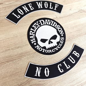 Puede incluir: Tres parches de motocicleta en blanco y negro. El parche superior dice "LONE WOLF" en texto blanco arqueado. El parche central es un parche circular de Harley-Davidson con un gráfico de calavera. El parche inferior dice "NO CLUB" en texto blanco arqueado.