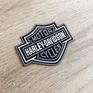 Op de afbeelding: Een zwart, wit en grijs Harley-Davidson Cycles-patch. De patch heeft het Harley-Davidson-logo met de woorden "MOTOR HARLEY-DAVIDSON CYCLES" in witte letters. De patch is rechthoekig met een schildachtige vorm.
