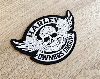 May include: Black and white embroidered patch featuring a skull with wings. The text "Harley Owners Group" is written in a circle around the skull.