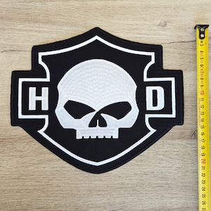 May include: Black and white embroidered patch with a skull and crossbones design. The patch features the letters "H" and "D" on either side of the skull.