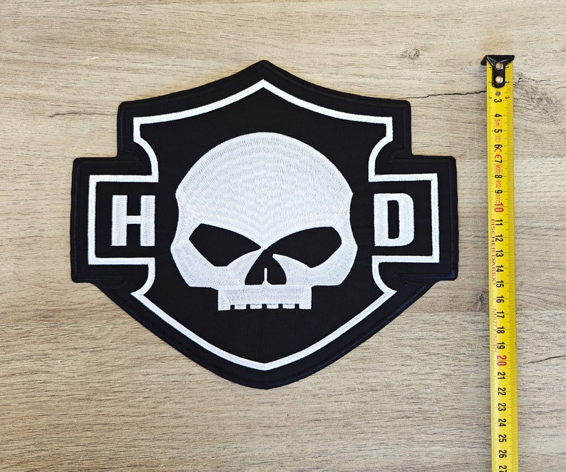 May include: Black and white embroidered patch with a skull and crossbones design. The patch features the letters "H" and "D" on either side of the skull.