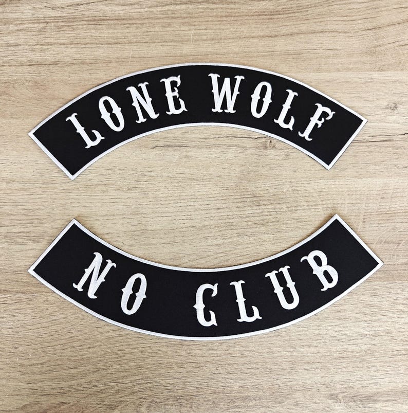 May include: Two black, arched patches with white text. The top patch reads "LONE WOLF" and the bottom patch reads "NO CLUB". The patches have a white border and are set against a light wood grain background.