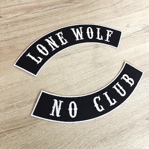 May include: Two black and white arched patches. The top patch reads "LONE WOLF" in white, stylized lettering. The bottom patch reads "NO CLUB" in white, stylized lettering. The patches are on a light brown wooden surface.