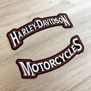 Op de afbeelding: Twee zwarte geborduurde patches met witte letters en oranje randen. De bovenste patch heeft de tekst "Harley-Davidson" en de onderste patch heeft de tekst "Motorcycles".