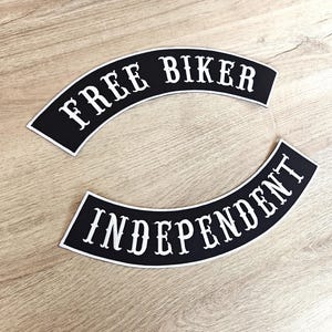 Puede incluir: Dos parches negros arqueados con texto blanco. El parche superior dice "FREE BIKER" y el inferior "INDEPENDENT". Ambos parches tienen un borde blanco. Los parches están sobre una superficie de madera marrón claro.