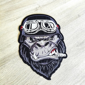 Può includere: Toppa ricamata raffigurante un gorilla con un casco nero e occhiali bianchi. Il gorilla ha un'espressione severa, un sigaro in bocca e la scritta "Hell Yeah" sul sigaro. La toppa è nera, grigia e bianca.