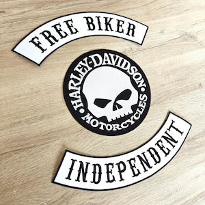 May include: Three motorcycle patches: "FREE BIKER" in a white arch, a black and white Harley-Davidson skull patch, and a white arch patch that reads "INDEPENDENT". The patches are on a light wood surface.