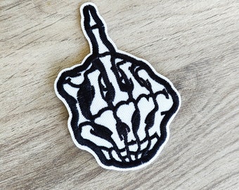 May include: Black and white embroidered patch of a skeleton hand giving the middle finger.