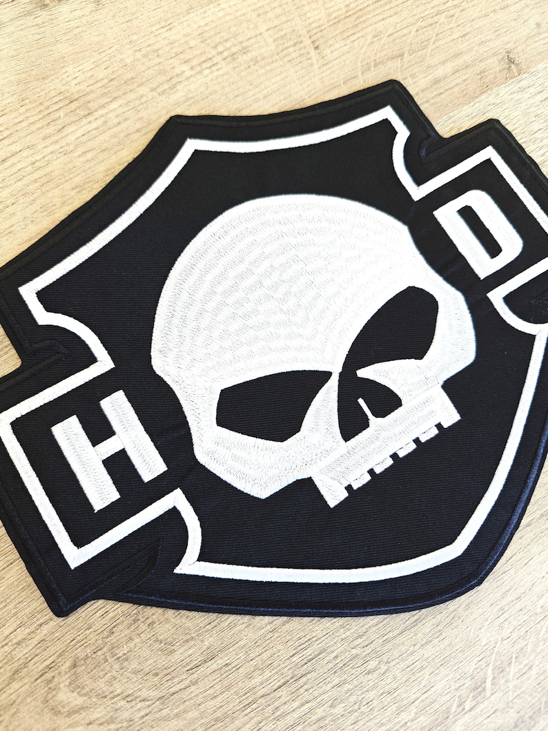 May include: Black and white embroidered patch with a skull and the letters "H-D" in a shield shape.