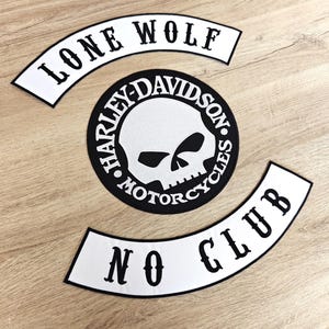 Puede incluir: Tres parches en blanco y negro sobre una superficie de madera. Los parches incluyen un logotipo circular de calavera Harley-Davidson y dos parches curvos con los textos "LONE WOLF" y "NO CLUB".