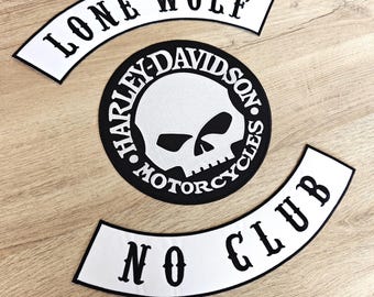 May include: Three black and white patches on a wooden surface. The patches include a circular Harley-Davidson skull logo, and two curved patches with the text "LONE WOLF" and "NO CLUB".