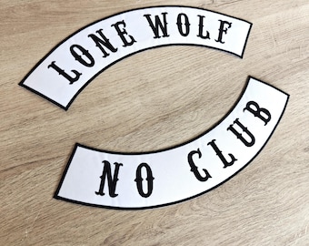 May include: Two white, curved patches with black text. The top patch reads "LONE WOLF" and the bottom patch reads "NO CLUB". The patches have a black border and are displayed on a light brown wooden surface.