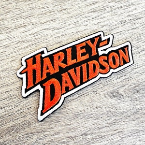 Peut inclure: Un patch brodé orange et noir avec le texte "Harley-Davidson" dans une police de caractères stylisée.