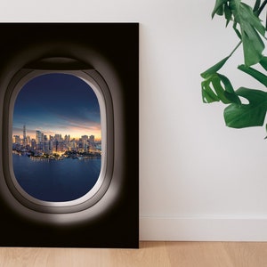 Puede incluir: Una fotografía de un horizonte urbano visto a través de la ventana de un avión. La ciudad está iluminada por la noche y el cielo es azul oscuro.