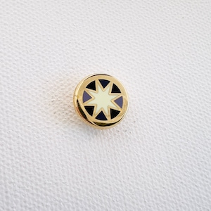 May include: A gold-colored pin with a white star in the center surrounded by a black and blue design.
