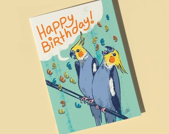 May include: A greeting card with a blue background and the text "Happy Birthday!" in orange and yellow. Two yellow-crested cockatiels are perched on a branch with confetti falling around them.