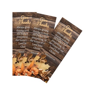 May include: Three rectangular wooden-textured cards with the words "Give Thanks" in gold script. The cards feature text from Ephesians 5:20, pumpkins, and fall leaves. The background is a rustic wood grain.