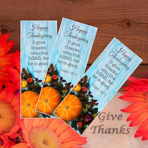 May include: Three Thanksgiving-themed bookmarks with a light blue wood grain background. Each bookmark features the text "Happy Thanksgiving" and a Bible verse. Pumpkins, apples, and fall foliage decorate the bottom. Orange flowers and the words "Give Thanks" are also visible.