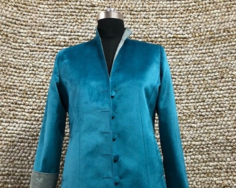 May include: Teal velvet coat with a mandarin collar and button-down front. The coat has long sleeves with gray cuffs and a slight A-line shape. The coat is displayed on a mannequin against a textured background.