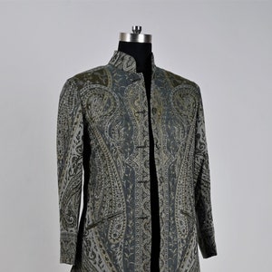 May include: A long, patterned coat in shades of gray and olive green, displayed on a mannequin. The coat features a paisley design and a mandarin collar. It has a button-up front and pockets. The coat is approximately 50 inches long.