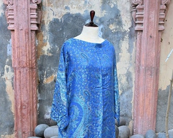 May include: A blue paisley print tunic dress on a wooden dress form. The dress features a boat neck, long sleeves, and a knee-length hemline. The fabric has a detailed pattern in shades of blue and teal.