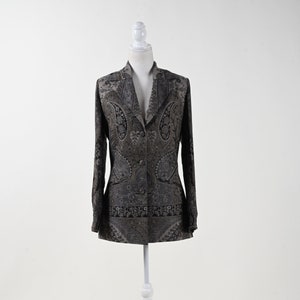 Può includere: Un blazer grigio scuro con un motivo paisley, esposto su un manichino bianco. Il blazer ha un colletto a revers, due bottoni e maniche lunghe. Il motivo paisley è visibile su tutto il capo.