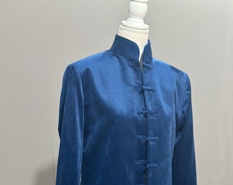 May include: A long, dark blue velvet coat with a mandarin collar and frog closures down the front. The coat is displayed on a mannequin and has long sleeves. The fabric appears soft and drapes elegantly. The style is reminiscent of traditional Asian garments.