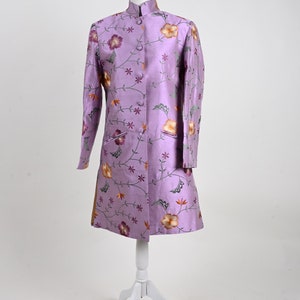May include: A lavender coat with a mandarin collar and floral embroidery. The coat is displayed on a white mannequin. The embroidery features orange, purple, and green flowers and vines. The coat has long sleeves and a button-up front.