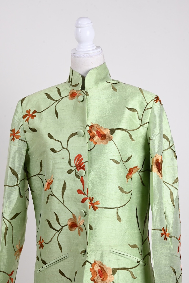May include: A light green jacket with a mandarin collar and floral embroidery. The jacket features a button-up front and two small pockets. The floral design includes orange and brown flowers with green stems and leaves.