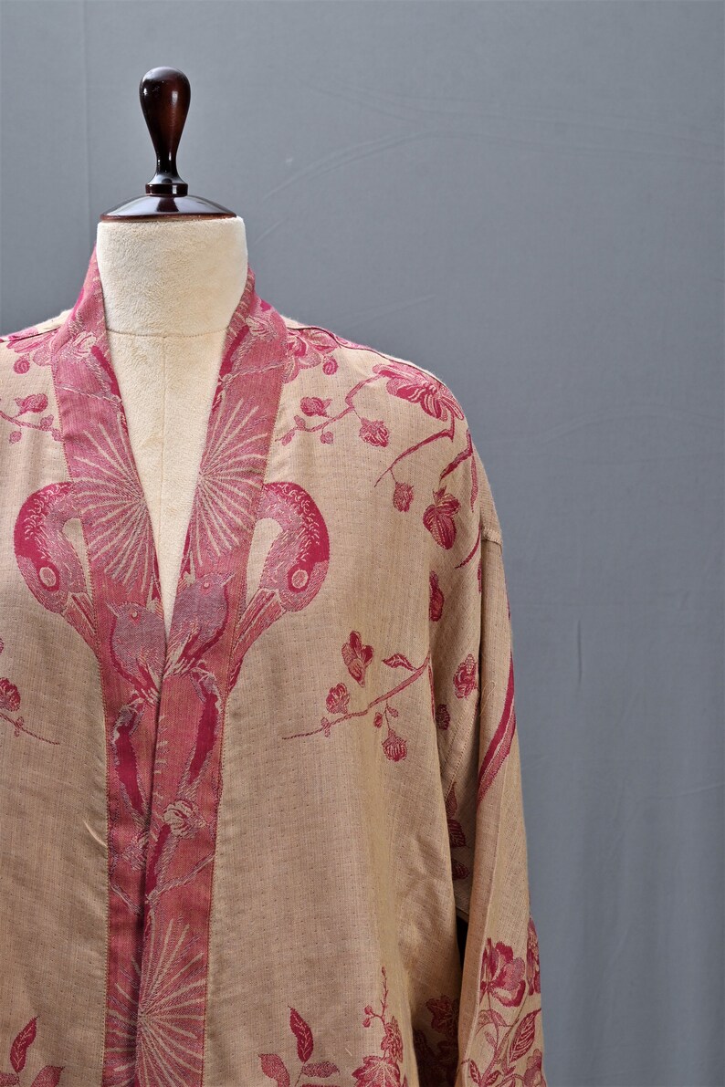 May include: A beige kimono-style robe with a floral and bird pattern in shades of red. The robe is displayed on a mannequin, showcasing the intricate design and flowing fabric. The robe's design features a repeating pattern of stylized birds and flowers.