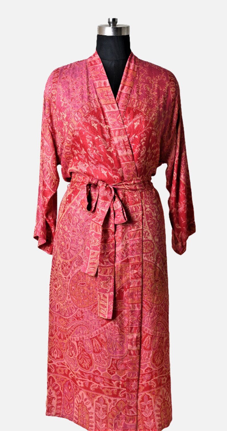 May include: A long, red patterned robe with a matching belt. The robe is displayed on a mannequin and features a detailed, all-over design in shades of red and pink. The fabric appears to be lightweight and flowing.