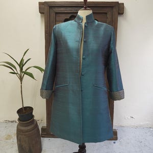 May include: A teal-colored, long-sleeved coat with a mandarin collar and button closure. The coat features two front pockets and decorative cuffs. The garment is displayed on a mannequin.