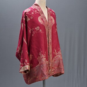 May include: A red kimono-style robe with a floral pattern in beige and gold. The robe is displayed on a mannequin, showcasing its loose fit and wide sleeves. The fabric appears lightweight and flowing.