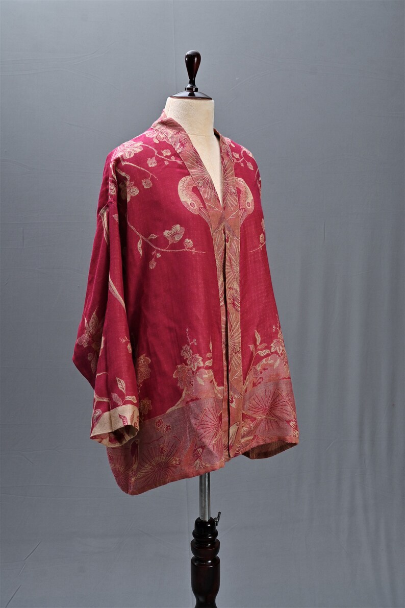 May include: A red kimono-style robe with a floral pattern in beige and gold. The robe is displayed on a mannequin, showcasing its loose fit and wide sleeves. The fabric appears lightweight and flowing.