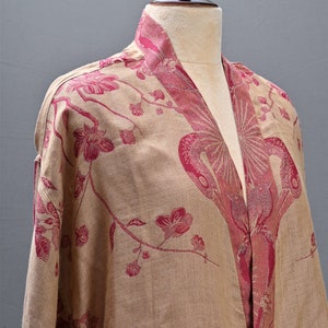 May include: A beige kimono-style robe with a floral pattern in shades of red. The robe is displayed on a mannequin, showcasing the intricate design and flowing fabric. The collar and edges are accented with a darker red.