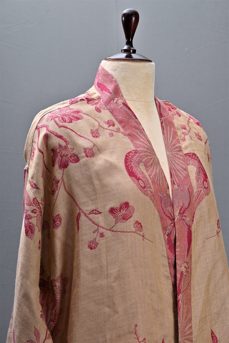 May include: A beige kimono-style robe with a floral pattern in shades of red. The robe is displayed on a mannequin, showcasing the intricate design and flowing fabric. The collar and edges are accented with a darker red.