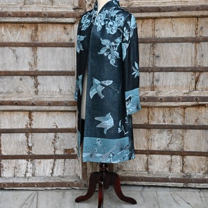 May include: A long, dark blue kimono-style robe with a floral and bird pattern in light blue. The robe is displayed on a wooden mannequin, showcasing its design and length. The background features a rustic wooden door.