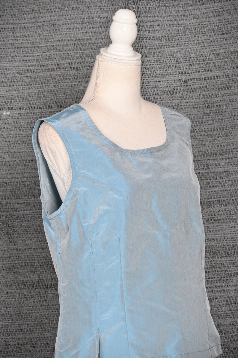 Pu&ograve; includere: Un top senza maniche azzurro chiaro con scollatura quadrata. Il tessuto ha una lucentezza sottile e un dettaglio di cucitura verticale sul davanti. Il top &egrave; esposto su un busto di manichino bianco su uno sfondo grigio strutturato.